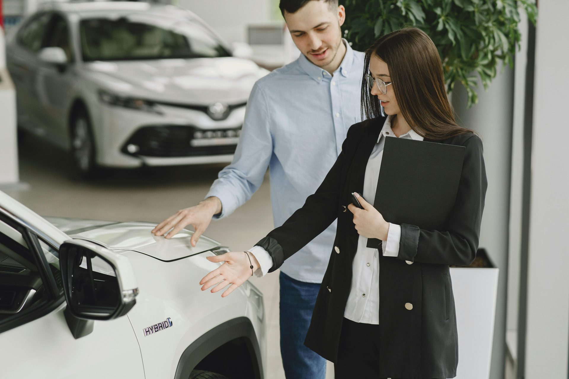 A man and saleswoman discussing a hybrid vehicle's features in an indoor showroom.