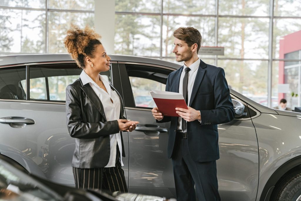 Une femme discute de l'achat d'une voiture avec un vendeur dans la salle d'exposition d'une concession automobile.
